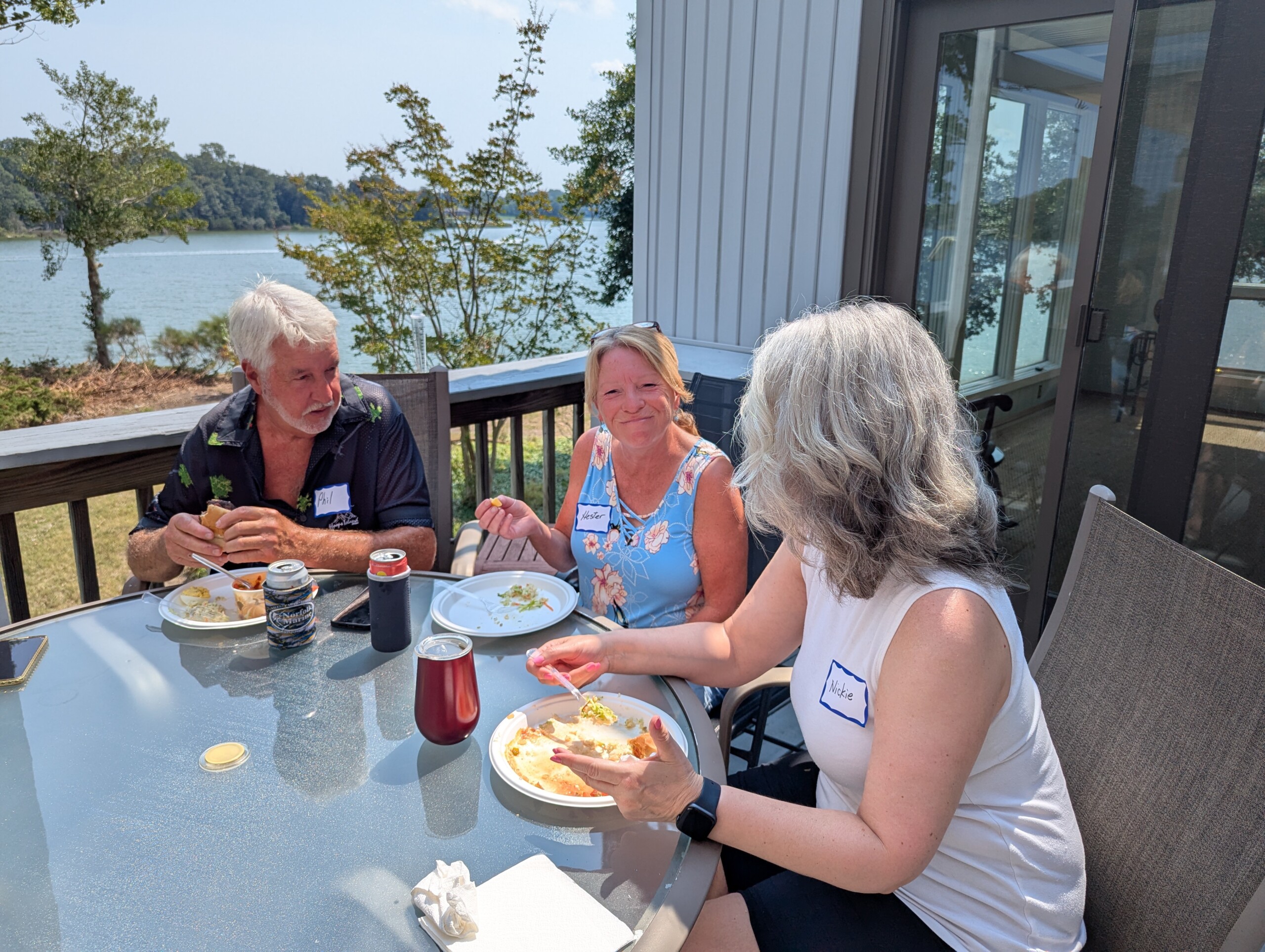 Three people eating outdoors by a lake.
